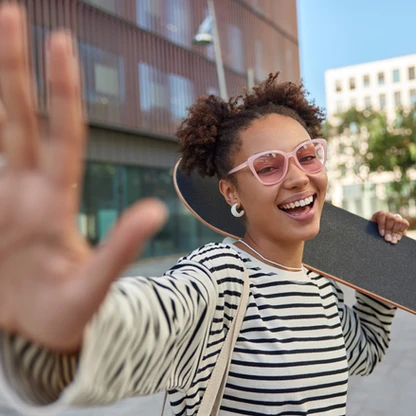 carefree-cheerful-woman-keeps-palm-forward-camera-smiles-positively-enjoys-riding-skateboa